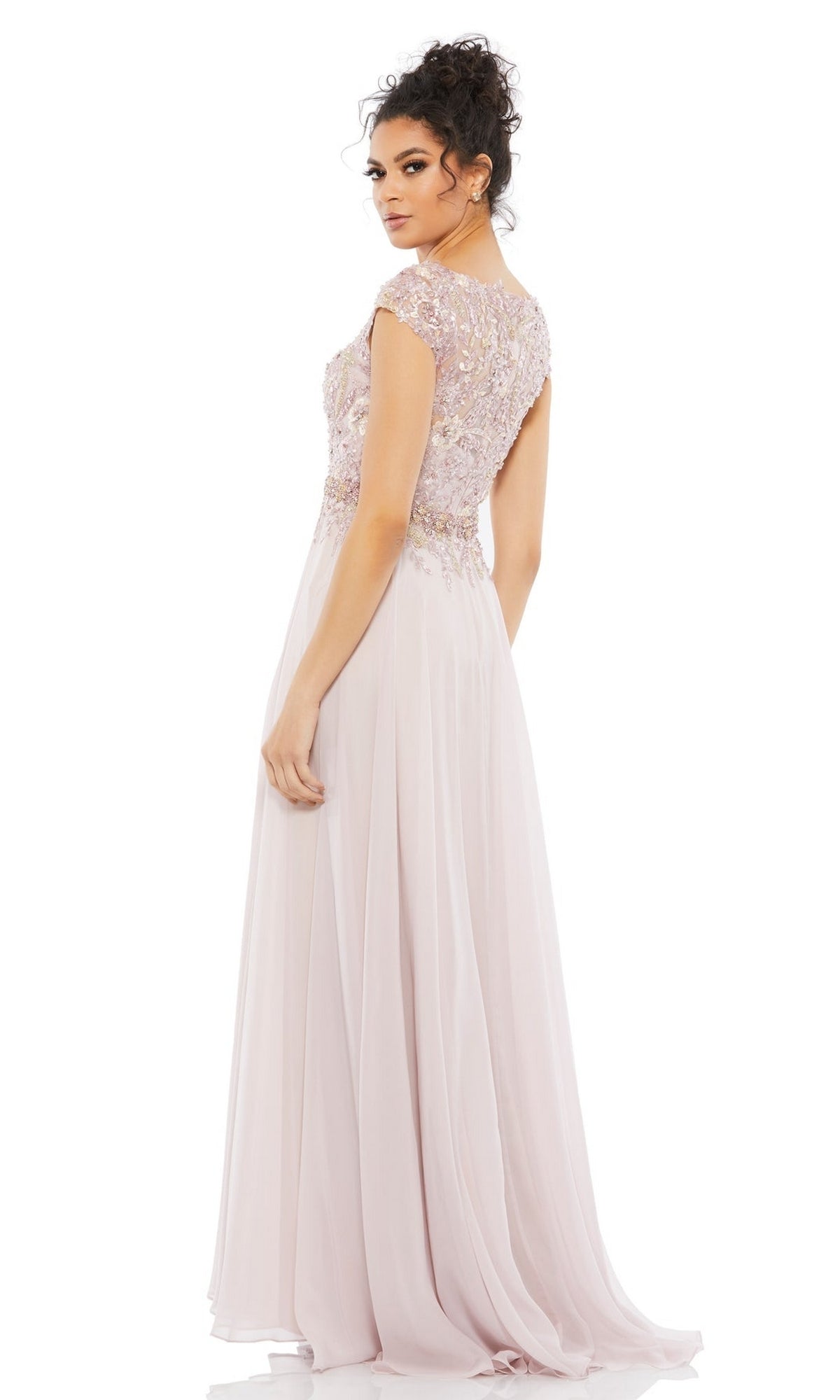 A woman in the Cap-Sleeve Long Formal Dress: Mac Duggal 79365, a floor-length light pink gown with an embellished bodice, stands facing backward and looks over her shoulder.